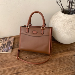 Détail d'un sac à main marron avec ferrures dorées sur table en bois et magazines