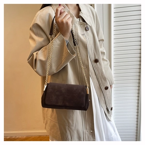 Detail of dark coffee suede crossbody bag with elegant gold chain strap on trench coat