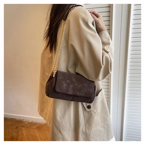 Detail of dark brown crossbody bag with gold chain strap and crisscross stitching