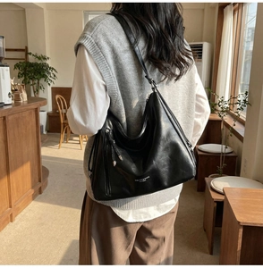 Detail of black faux leather shoulder bag featuring silver tassels and zip hardware