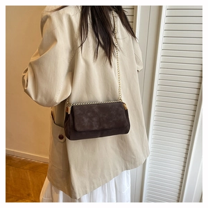 Brown suede crossbody bag with gold chain strap shown on a woman wearing a blazer