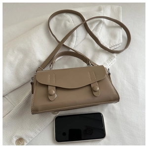 Detail view of khaki retro crossbody bag on white knit background with smartphone for scale