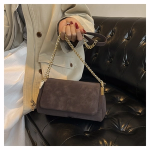 Detail of brown suede crossbody bag with gold chain strap and cross stitching on cover