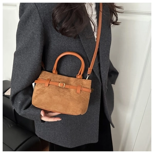Sac seau vintage en daim marron avec sangle en cuir porté sur un blazer en tweed