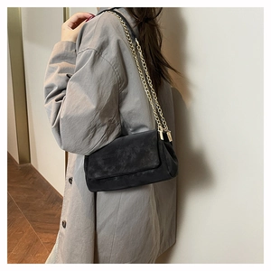 Detail of black suede shoulder bag with elegant gold chain strap and minimalist design