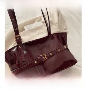Detail van bordeauxrode glanzende leren tas met oogjesband en metalen gespen