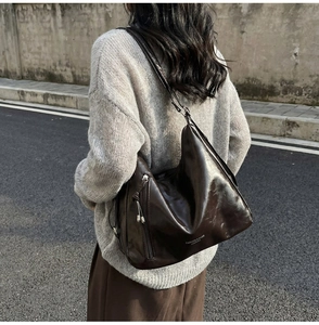 Outdoor shot of a vintage brown glossy leather shoulder bag with metallic zipper detail