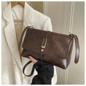 Détail du sac vintage marron foncé avec boucle dorée sur un blazer blanc texturé