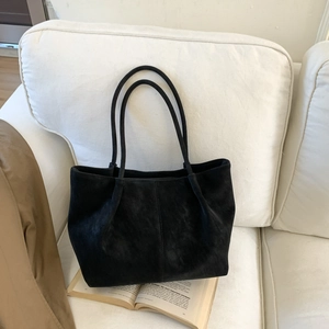 Minimalist black matte tote bag with vertical stitching on a white sofa setting