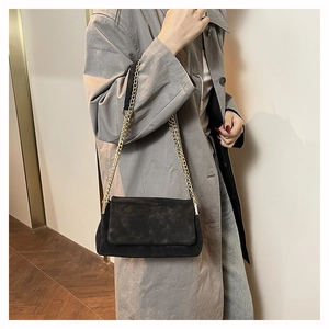 Detail of black suede shoulder bag with gold chain strap and cross stitching design