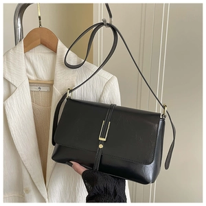 Détail du sac bandoulière en cuir noir avec sangle verticale et boucle dorée