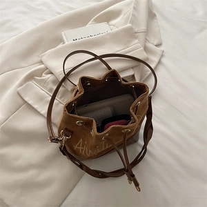 Brown drawstring bucket bag in mixed leather and suede with a woven shoulder strap