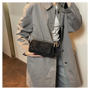 Detail of a black quilted crossbody chain bag styled with a grey trench coat and denim