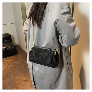Detail of black crossbody bag with golden chain strap on a long coat back view