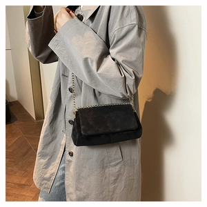Detail of black crossbody bag with matte finish, cross stitching and gold chain strap