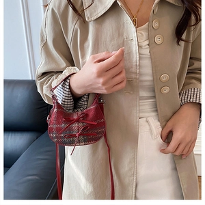 Detail of red plaid mini crossbody bag with double bows worn over a beige coat