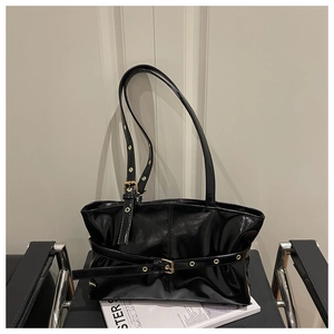 Close-up of black glossy shoulder bag with metallic eyelets and gold buckle details
