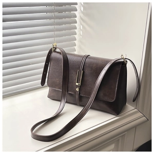 Détail d'un sac à bandoulière vintage marron avec fermoir doré sur rebord de fenêtre