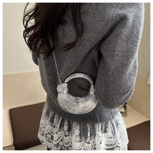 Détail latéral d'un sac demi-lune argenté avec texture ondulée et poignée en anneau