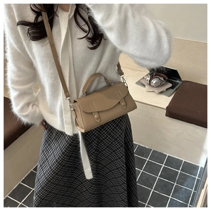Close-up of a khaki vintage crossbody bag with flap and decorative straps on a desk