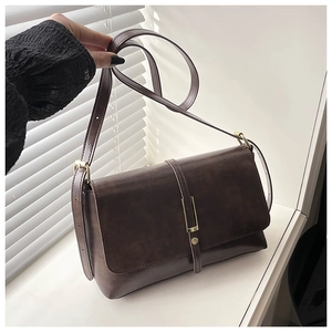 Détail d'un sac bandoulière vintage en similicuir marron foncé avec boucle sur un rebord
