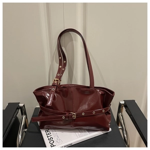 Detail of burgundy glossy leather shoulder bag with decorative metal eyelets and buckles
