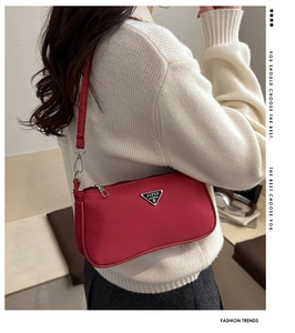 Detail of red nylon shoulder bag with silver triangle logo worn on white sweater
