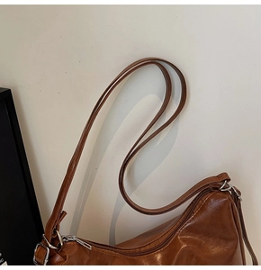 Close-up of brown PU leather shoulder bag featuring silver metal buckle and adjustable strap