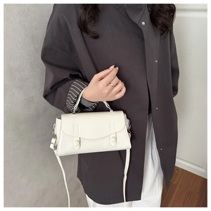 Detail of cream white leather handbag with flap and twin round buckles on dark coat