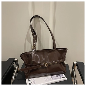 Detail of dark brown glossy leather tote bag with metal buckle on a minimalist chair
