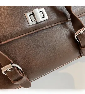Detail of brown leather grain texture and silver metal twist lock on a vintage pillow bag