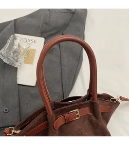 Detail of dark brown faux suede handbag showing smooth leather handle and gold hardware