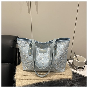 Detail of light blue quilted star tote bag with metallic logo on textured fabric surface