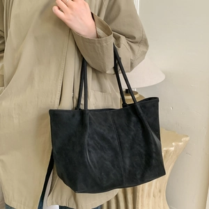 Detail of a black matte leather tote bag styled with a beige trench coat for a casual look