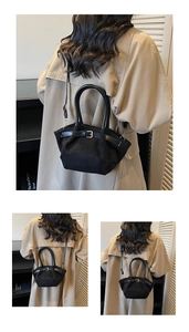 Detail of black suede shoulder bag with buckle strap on model wearing khaki coat