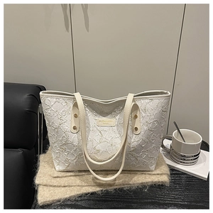Detail of floral embroidery on cream pleated tote bag with metal brand logo on the front