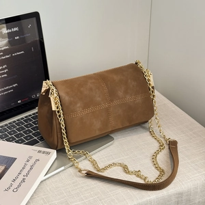 Brown suede crossbody messenger bag with cross stitching and gold chain strap on laptop