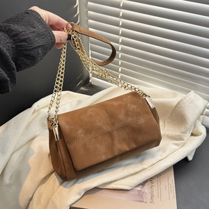 Brown suede tote bag with cross-stitch flap and gold chain strap in a studio setting