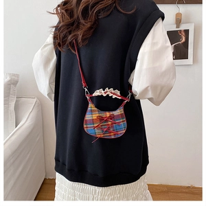 Detail of a plaid mini crossbody bag with red bows and lace handle on a shoulder