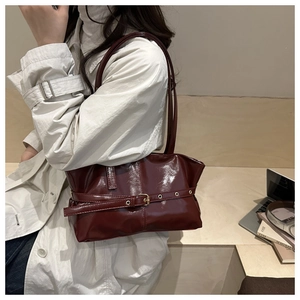 Detailed close-up of dark red patent leather shoulder bag with buckle strap on model
