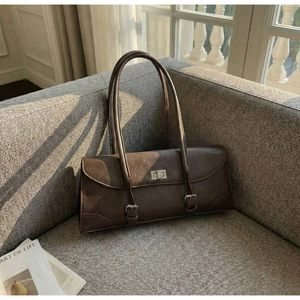 Close-up of vintage brown leather underarm bag with silver twist lock on gray sofa