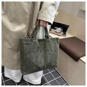 Close-up of dark green corduroy tote bag featuring TOTE BAG text in a modern office setting
