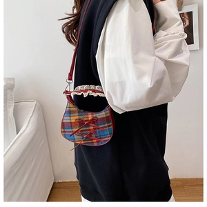 Detail of checkered shoulder bag with red bows and white lace trim shown on model