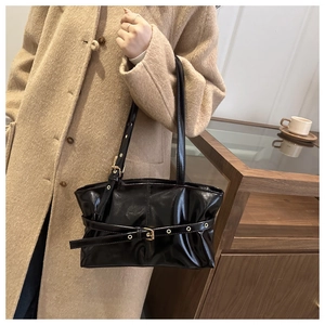 Detail of black patent leather underarm bag with adjustable metal buckle strap