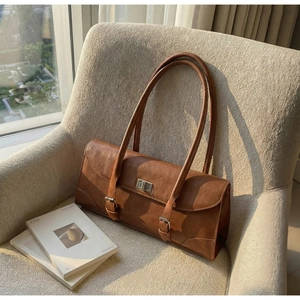 Detail of vintage brown baguette bag with metal twist lock on beige textured sofa