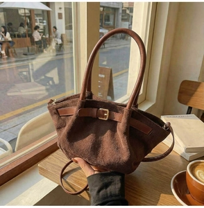 Detail of dark brown suede handbag with golden buckle on a wooden cafe table