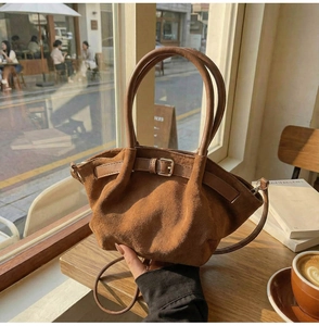 Detailed view of brown suede dumpling handbag featuring leather buckle on a wooden table