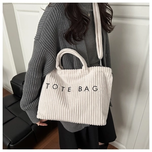 Detailed texture of white corduroy tote bag with embroidered TOTE BAG lettering and strap