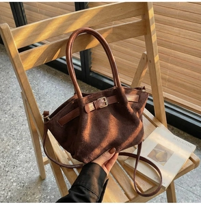 Detailed macro view of a brown suede handbag with decorative buckle and cylinder handles