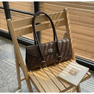 Detailed view of coffee brown baguette bag with silver twist lock on wooden chair